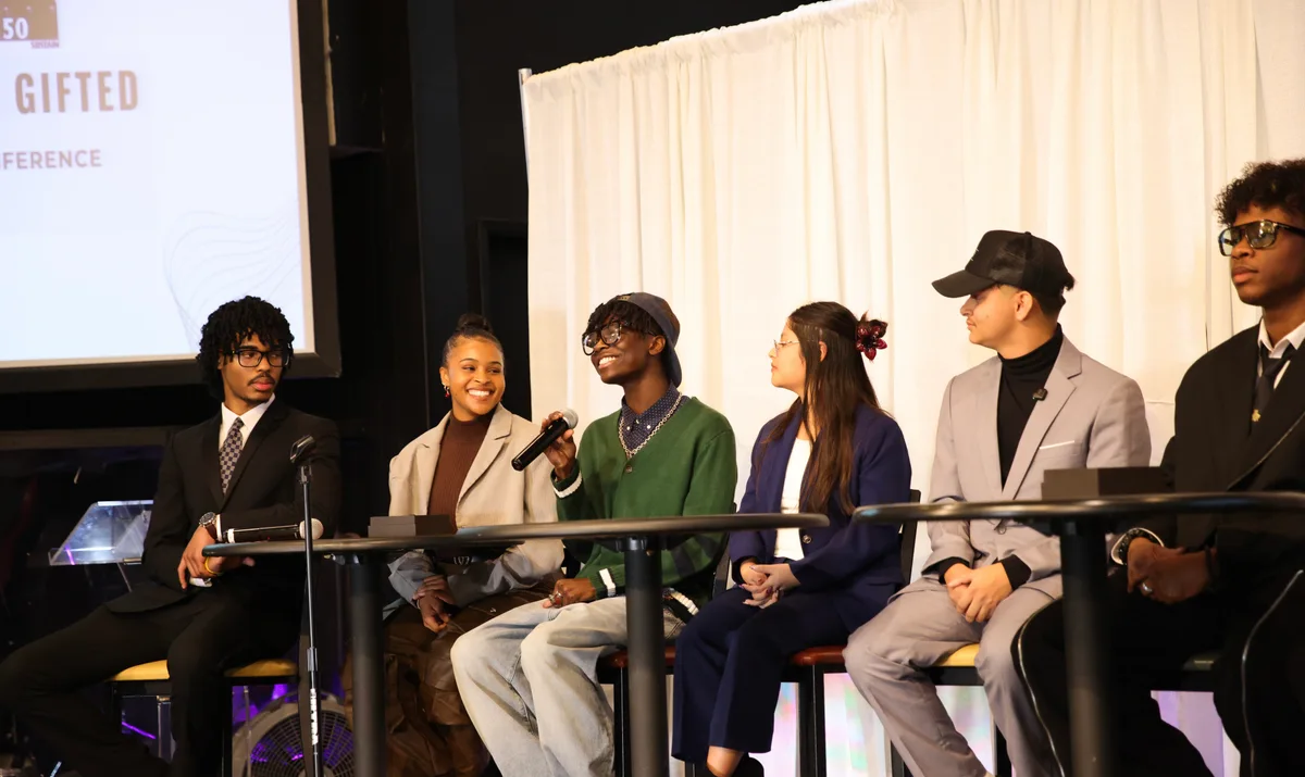 Wide shot of full December 2025 panel, Jaxton moderating with five panelists